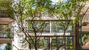 Un edificio moderno con un árbol en primer plano, una bicicleta estacionada afuera y una entrada visible.