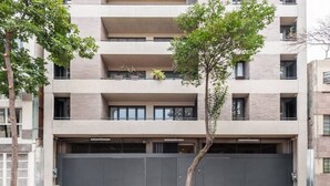 Un immeuble résidentiel à plusieurs étages, doté d’un grand portail de garage central, de balcons et d’un arbre au premier plan.