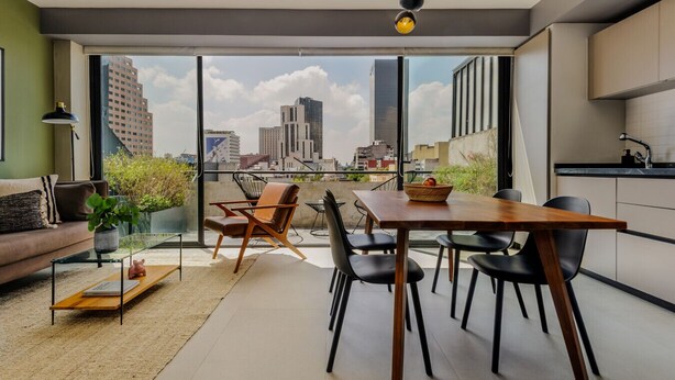 Un appartement moderne doté d’un coin repas, d’une cuisine et de grandes fenêtres offrant une vue sur la ville.