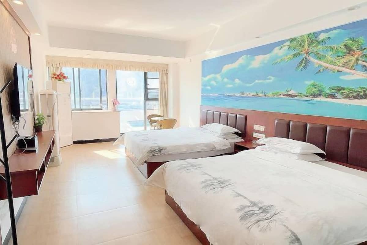 A hotel room with two beds, a large window, a painting of a tropical beach, and a TV on the left side.