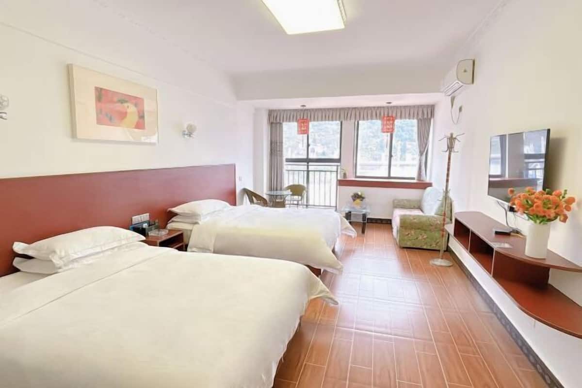 A hotel room with two beds, a TV, a small table with a vase of flowers, and a window with curtains.