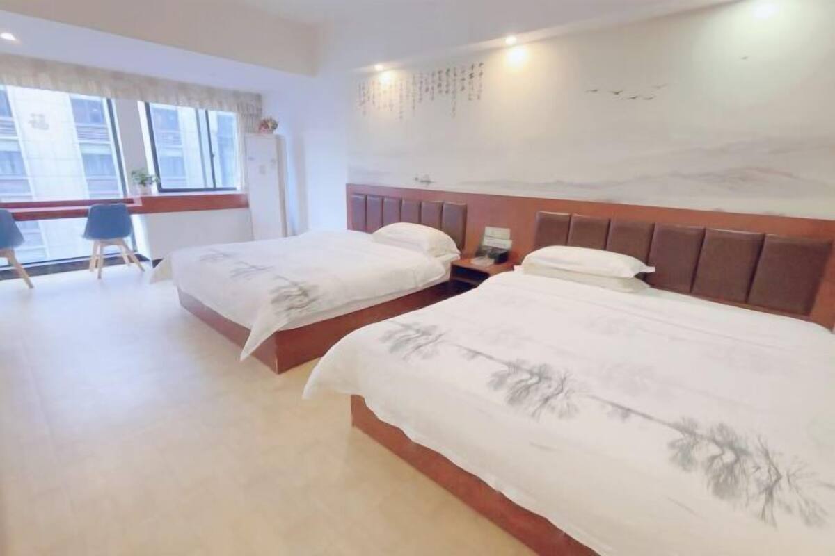 A hotel room with two beds, a desk, and a window with a view of buildings.