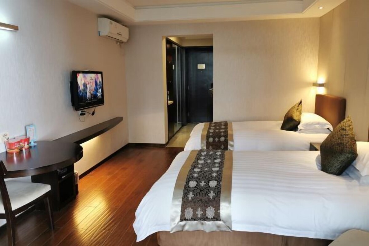 A hotel room with two beds, a desk, a TV, and a door leading to another room.