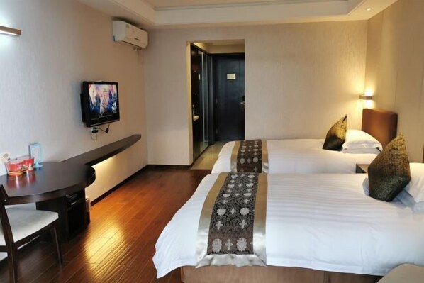 A hotel room with two beds, a desk, a TV, and a door leading to another room.