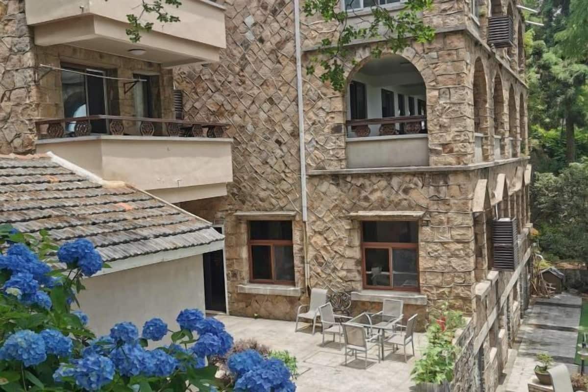 Un immeuble à plusieurs étages, doté d’une façade en pierre, de balcons et d’un espace extérieur aménagé pour s’asseoir.