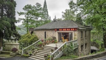 A small stone building with a staircase leading up to the entrance, surrounded by lush greenery and trees.