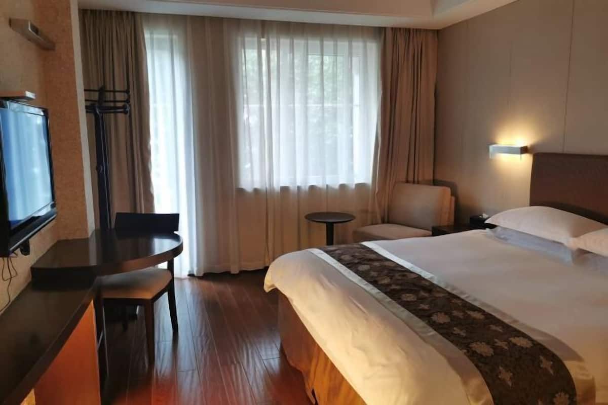 Une chambre d’hôtel équipée d’un lit, d’un bureau, d’une chaise, d’une télévision et d’une fenêtre avec des rideaux.