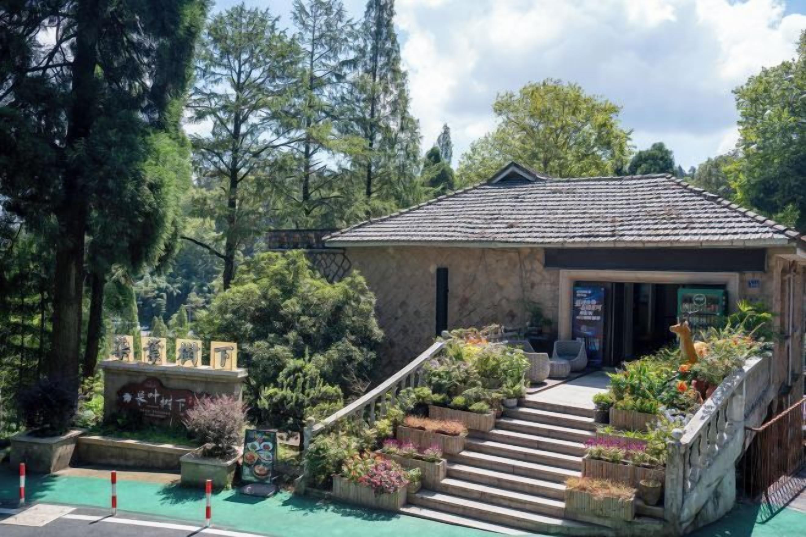 A stone building with a tiled roof, a staircase leading to the entrance, and a garden area with various plants and flowers.