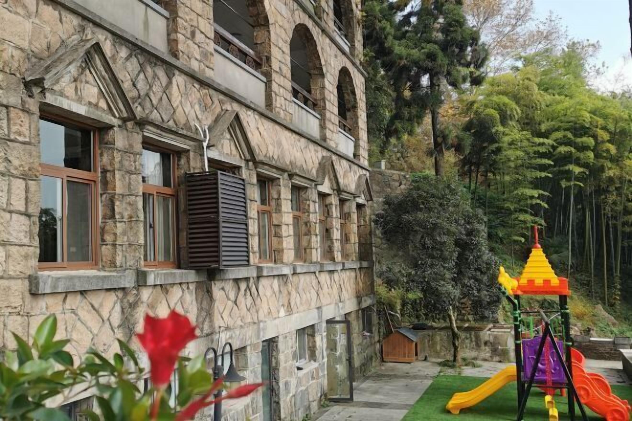 Um edifício de pedra com janelas em arco e um parquinho com escorregadores e estruturas de escalada.