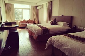 A hotel room with two beds, a sofa, a desk, and a large window.