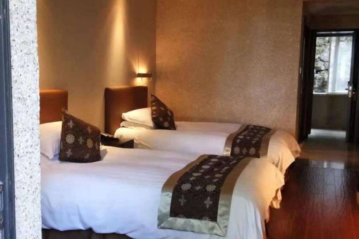 Une chambre d’hôtel avec deux lits, chacun équipé d’un oreiller et d’une couverture. On y trouve une lampe fixée au mur et une porte donnant sur un espace extérieur.