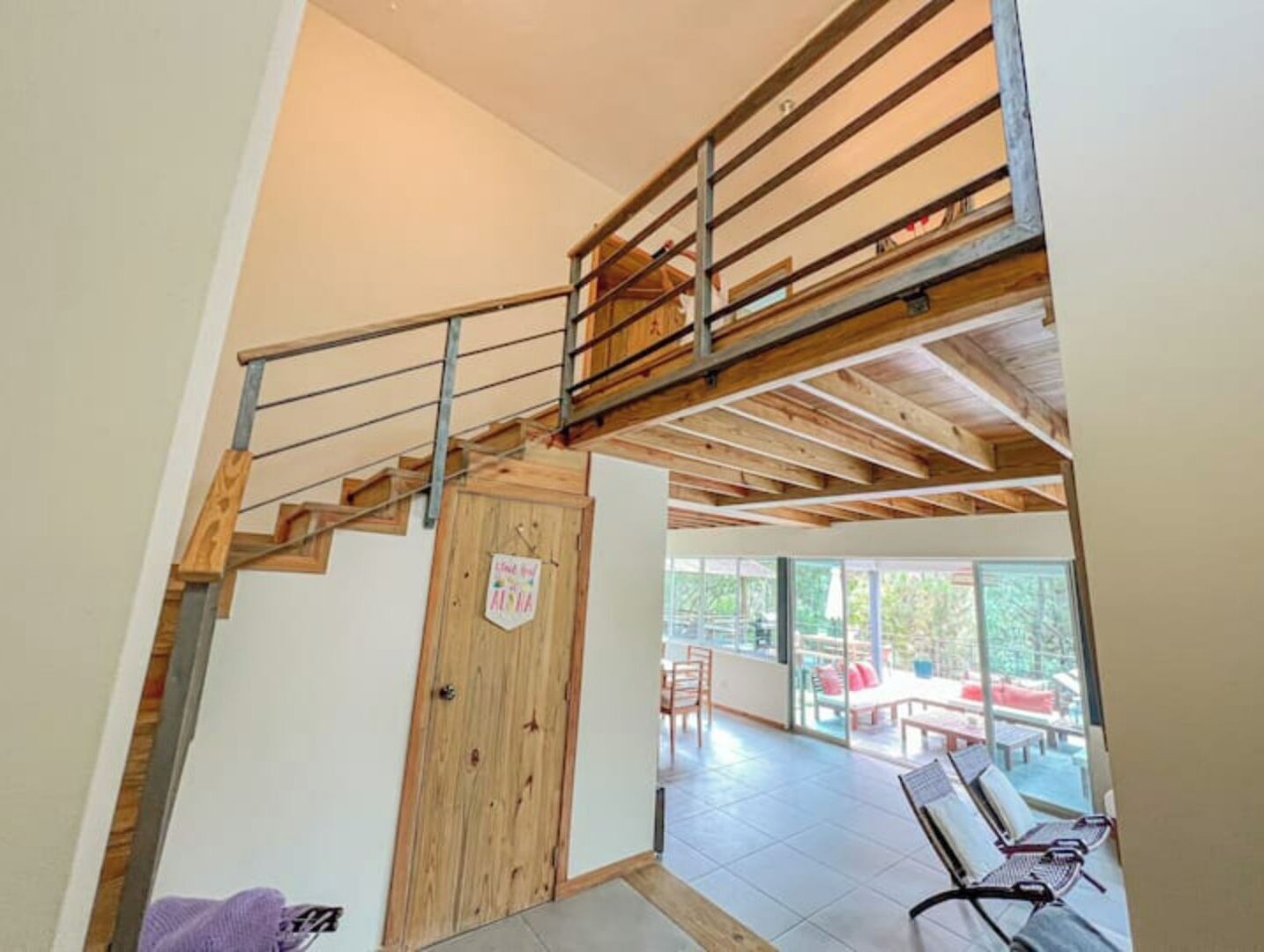 Un escalier en bois mène à un niveau supérieur, offrant une vue sur un espace patio extérieur.