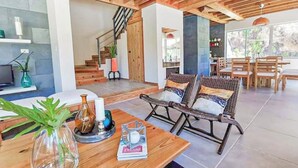 A spacious living area with a wooden ceiling, a dining table with chairs, and a staircase leading to an upper level.