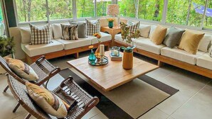 A spacious living room with a large window, a sofa set, a coffee table, and wicker chairs.