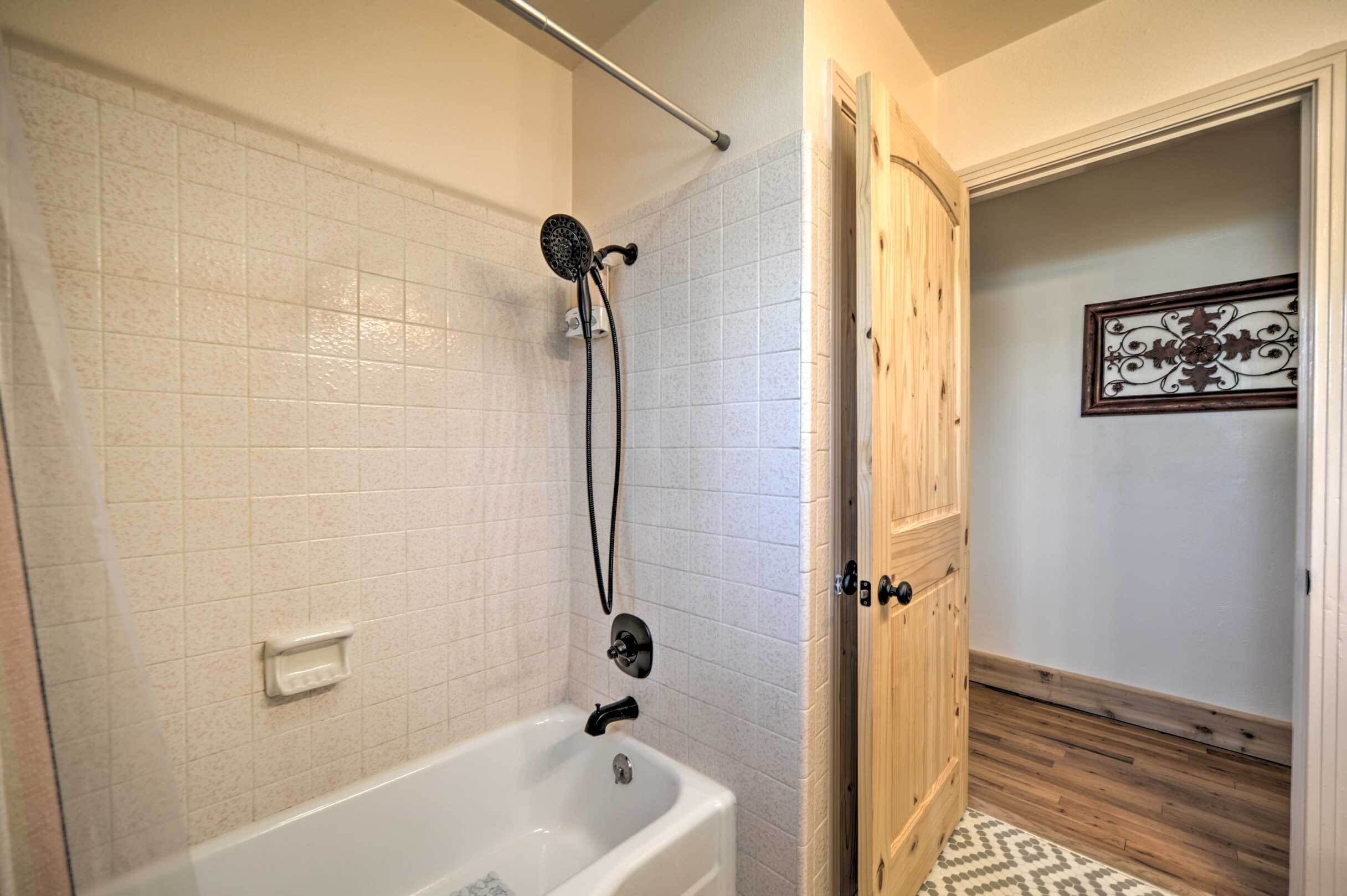 A bathroom with a white tiled shower, a white bathtub, and a wooden door.