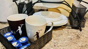 Een keukentrap met een koffiezetapparaat, een mand vol koffiekapsules en een muggenhouder met verschillende mokken.