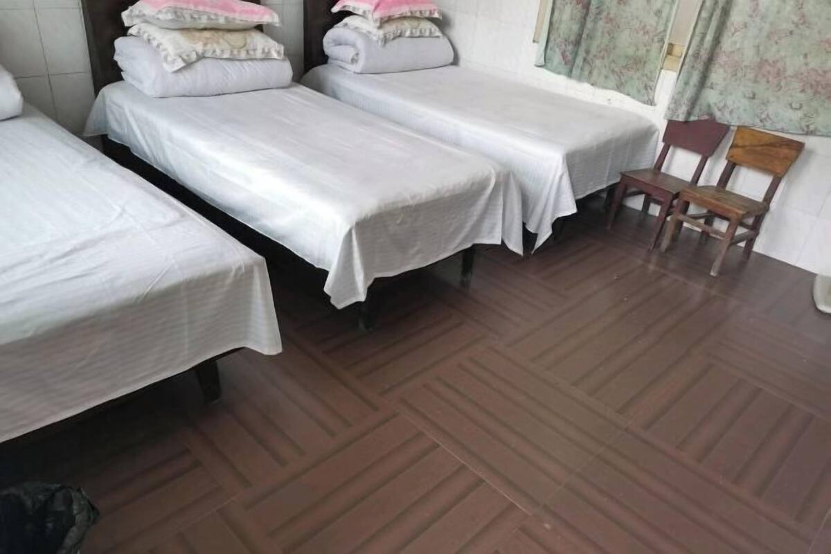 Een kamer met drie enkele bedden, een houten stoel en een gordijn met een patroon.