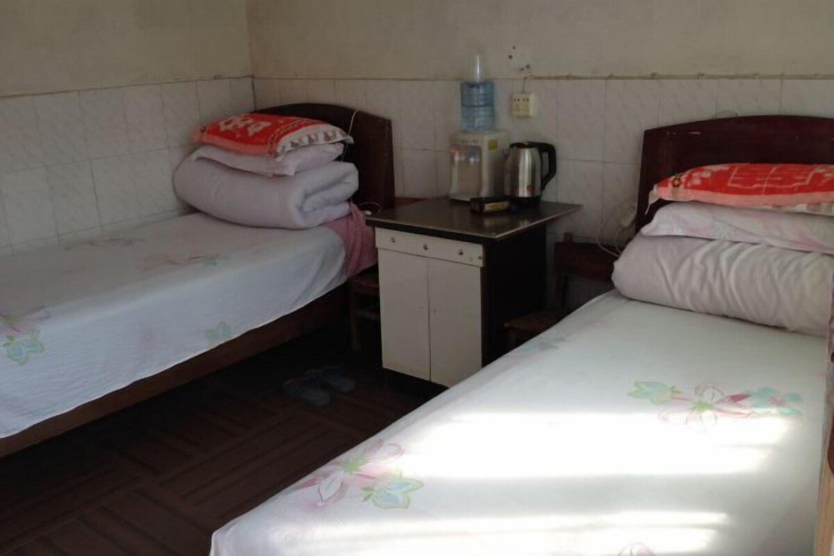 Une petite chambre simple, avec deux lits simples, une petite table et une bouilloire, ainsi qu’un distributeur d’eau.