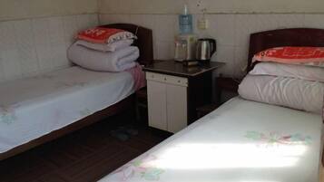 A small, simple room with two single beds, a small table with a kettle, and a water dispenser.