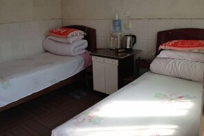 Une petite chambre simple, avec deux lits simples, une petite table et une bouilloire, ainsi qu’un distributeur d’eau.