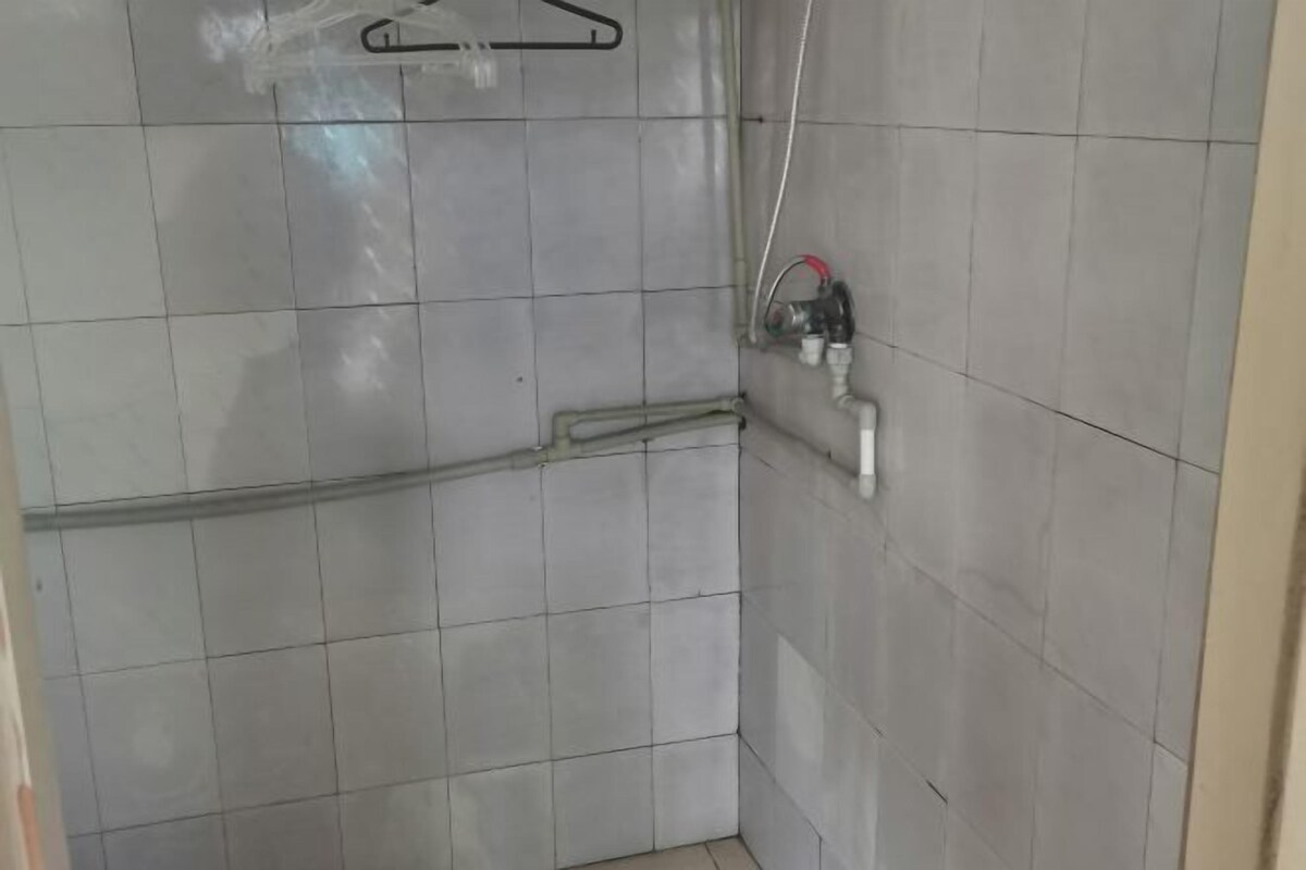 Une zone de douche carrelée, équipée d’un flexible et d’un robinet.