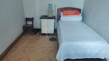 A small, single-bed room with a wooden chair, a white cabinet, and a water dispenser.