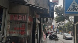Une vue de rue avec l’entrée d’un magasin, un panneau indiquant un passage pour piétons et des véhicules stationnés.