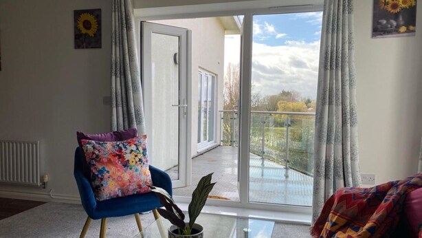 A modern living room with a blue armchair, a glass coffee table, and a view of a balcony.