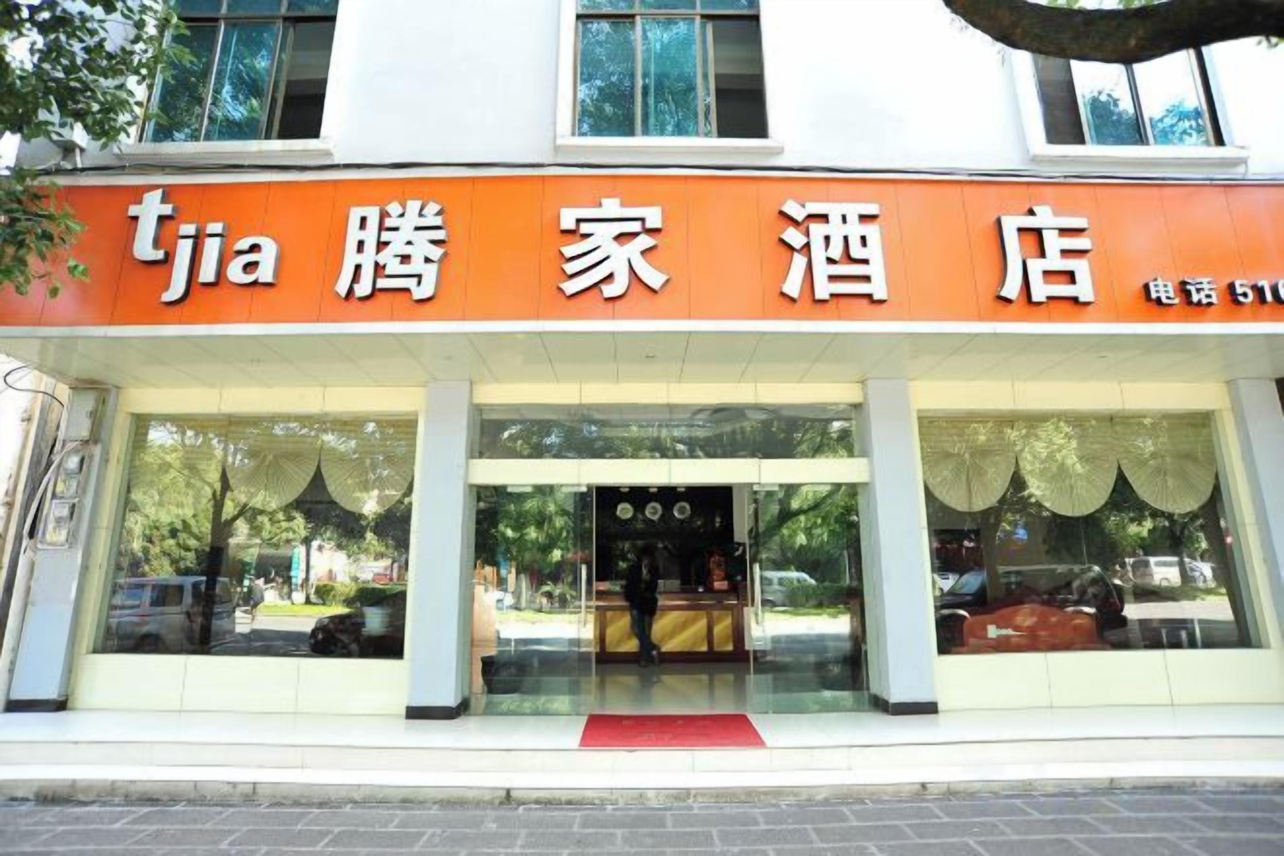 Un hotel con un llamativo letrero naranja, grandes ventanales y una alfombra roja en la entrada.