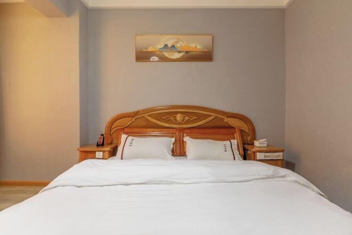 A neatly made bed with a wooden headboard, a bedside table with a lamp, and a painting on the wall.