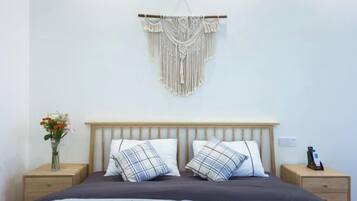 A bedroom with a wooden headboard, two bedside tables, a macrame wall hanging, and a vase with flowers.
