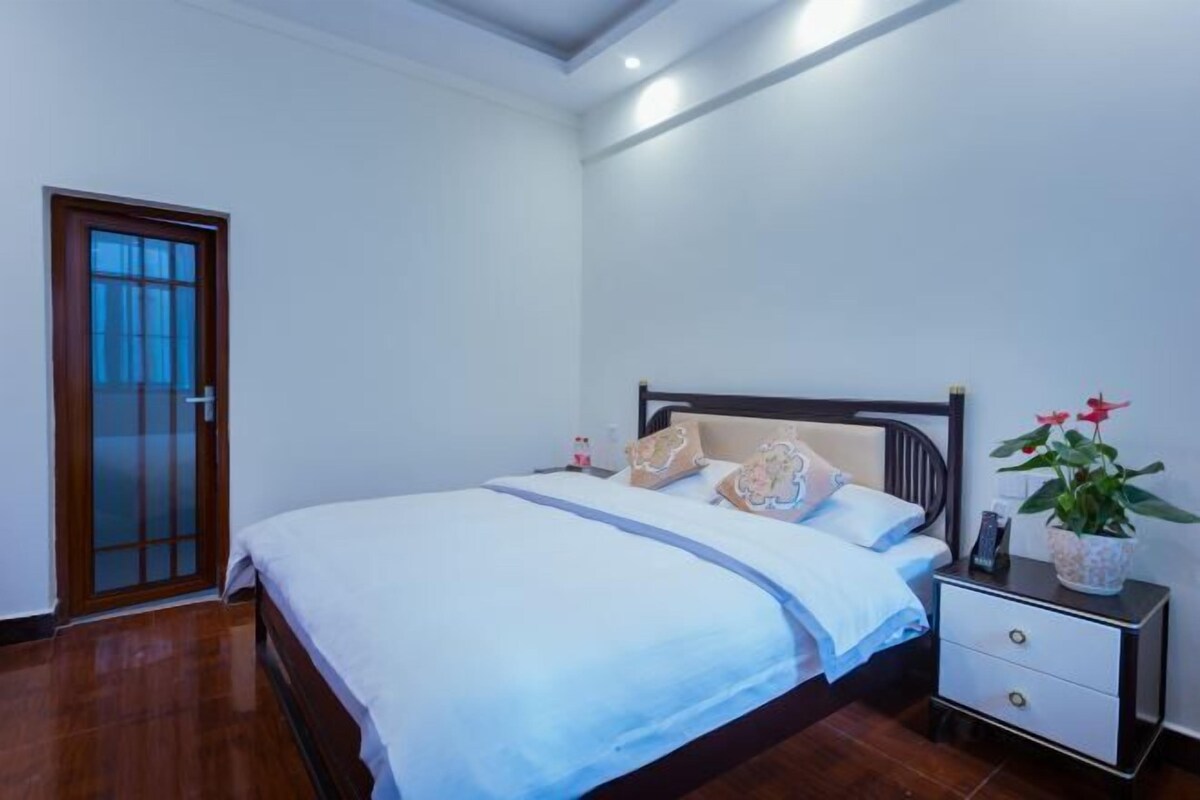 A bedroom with a bed, bedside table, and a potted plant.