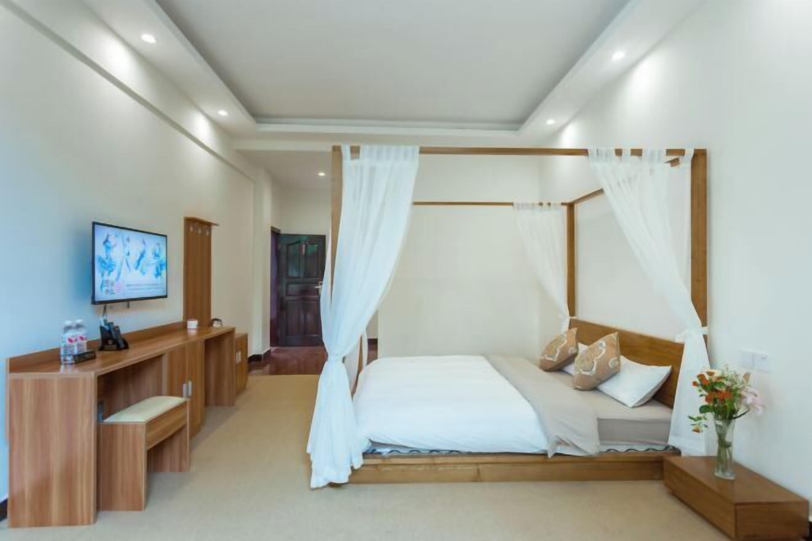 A bedroom with a canopy bed, a desk with a chair, and a television on the wall.