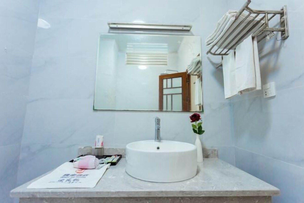 A bathroom with a white sink, a mirror, a towel rack, and a vase with a single flower.