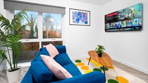 Un soggiorno moderno con un divano blu, un piccolo tavolino in legno, un tappeto colorato e un grande poster cinematografico al muro.