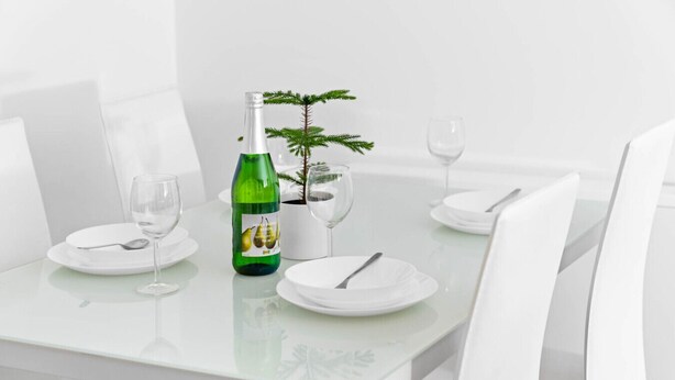 Un tavolo da pranzo apparecchiato con piatti bianchi, posateria e bottiglie verdi, con una piccola pianta in vaso.