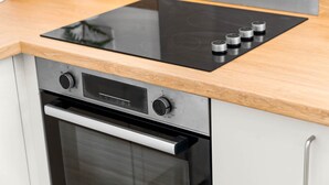 Cucina con piano cottura integrato e forno, piano di lavoro in legno e pensili in acciaio inossidabile.