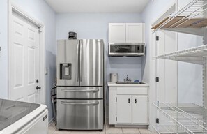 A compact kitchen with a stainless steel refrigerator, microwave, and white cabinets.