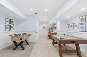 A room with two foosball tables, a desk, and framed pictures on the walls.