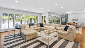 Una sala de estar moderna con un amplio sofá beige en forma de L, una mesa de centro de vidrio y un tapete a rayas.