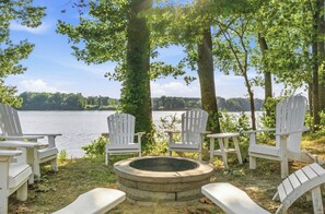 A lakeside seating area with Adirondack chairs and a fire pit.