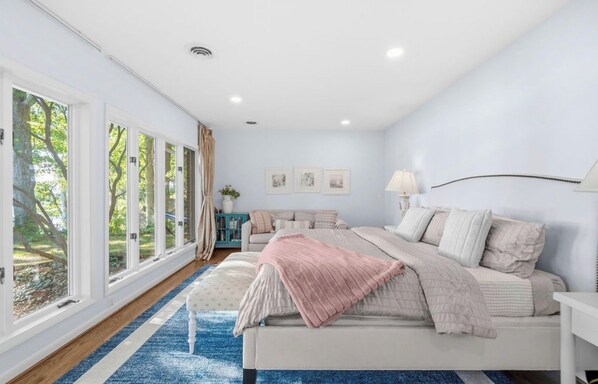 Une chambre à coucher avec un grand lit, une table de chevet, une lampe et une fenêtre avec des rideaux.