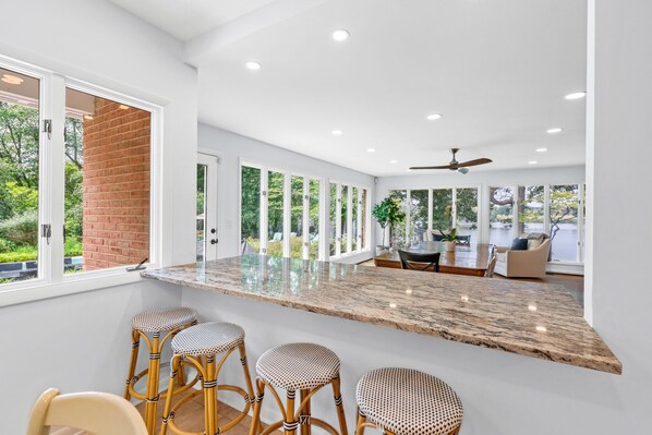 A modern kitchen with a large island, bar stools, and a dining area with a view of the outdoors.