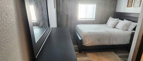Une chambre à coucher comprenant un lit, une commode, une fenêtre et des lambris en bois sur les murs.
