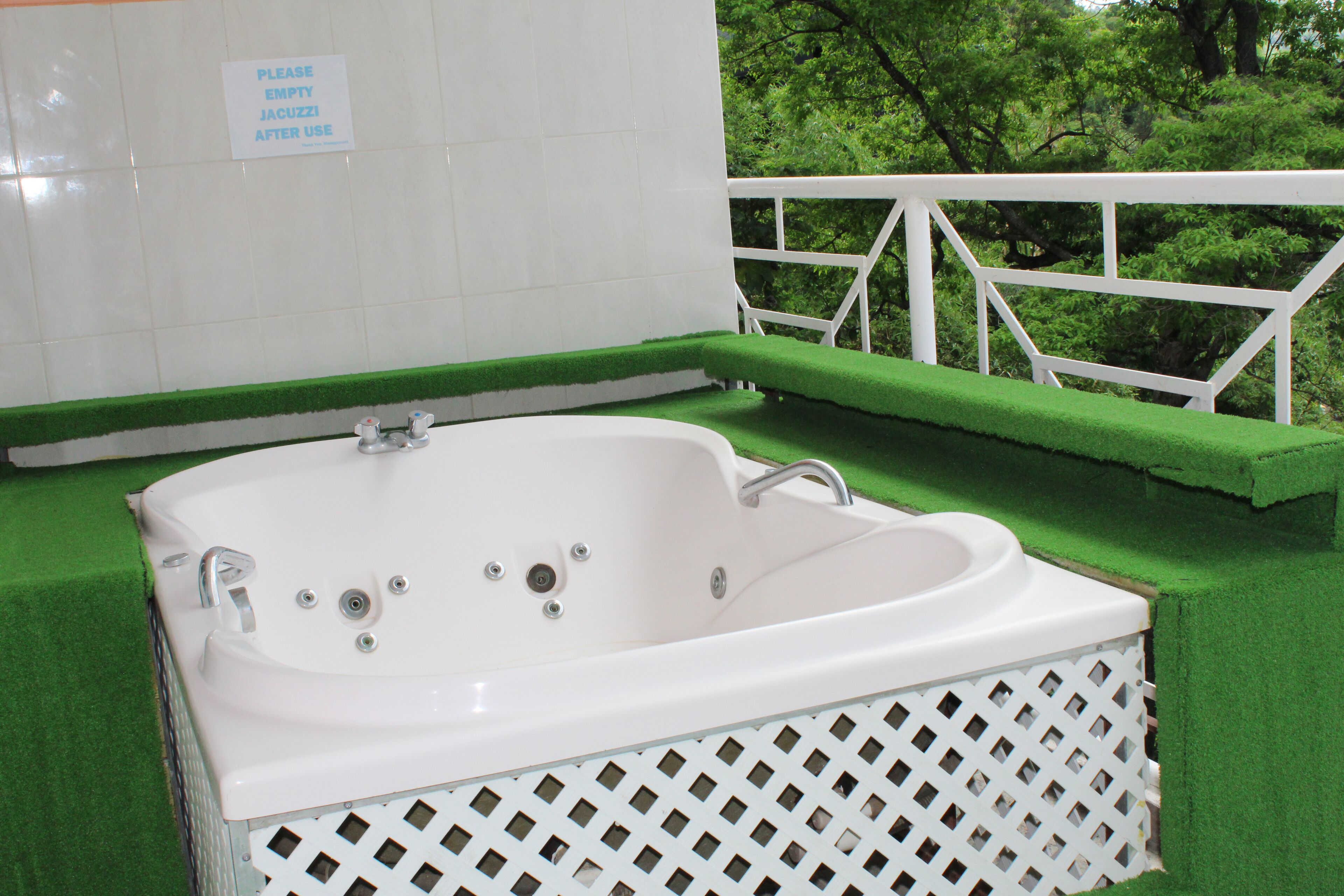 Una bañera blanca con borde verde, una barandilla blanca y un letrero que indica vaciar el jacuzzi después de su uso.