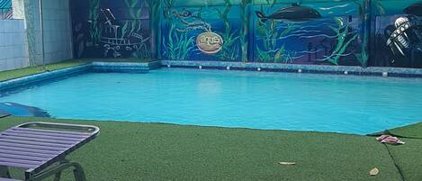 A swimming pool with an underwater mural, a covered area with a railing, and a lounge chair.