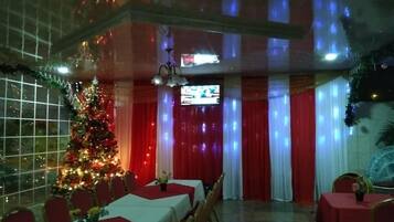 A dining area with tables set for a meal, a Christmas tree, and a television screen in the background.
