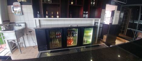 A bar area with a stainless steel sink, a refrigerator with multiple shelves, and a variety of bottles and glasses.