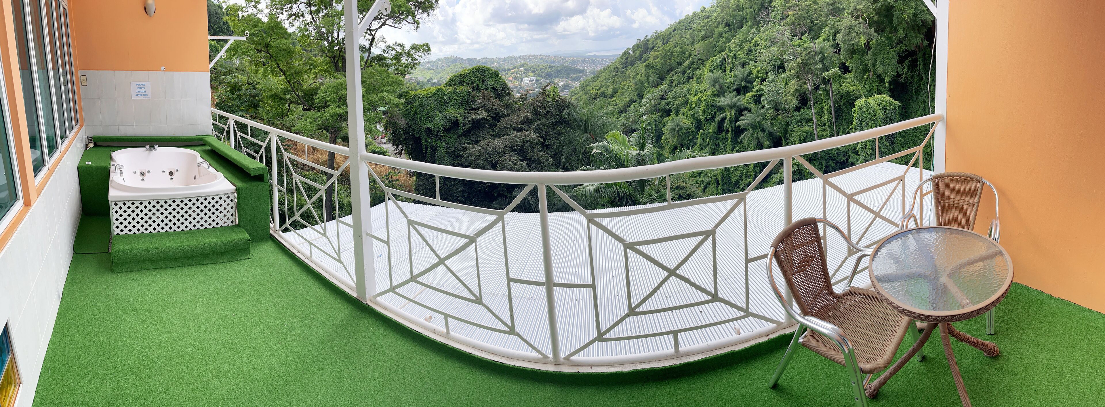 A balcony with a green artificial turf floor, a white bathtub, and wicker furniture.