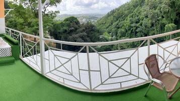 A balcony with a green artificial turf floor, a white bathtub, and wicker furniture.